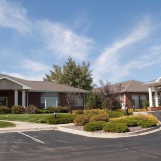 A suburban building with a landscaped garden and parking area under a partly cloudy sky.