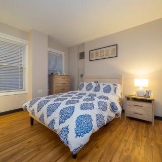 A cozy bedroom with a neatly made bed, nightstand, lamp, and dresser.