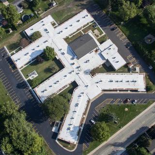 Aerial view of a cross-shaped building surrounded by parking lots and greenery.