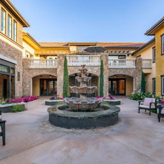 A beautifully designed Mediterranean-style courtyard featuring a central fountain surrounded by colorful flowers and elegant architecture.