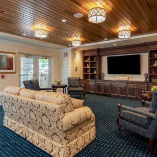 A cozy living room featuring elegant furniture, a large television, and wooden ceiling details.