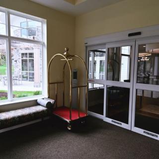 A hotel lobby with a bell cart and a bench near glass doors.