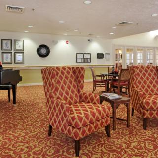 A cozy lounge area featuring patterned chairs, a piano, and warm lighting.