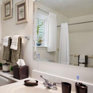 A tidy bathroom with a large mirror, neatly arranged towels, and decor including a small indoor plant.