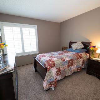 A cozy bedroom with a single bed covered in a colorful quilt, a dresser, and a lamp next to the window.