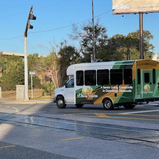 A colorful shuttle bus navigating an urban area, with a billboard in the background.