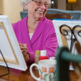 An elderly woman joyfully engaged in a painting activity, surrounded by art supplies.