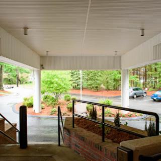 A view from under a covered area, looking towards a parking lot surrounded by greenery.