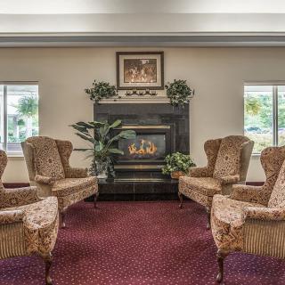A cozy living room with a fireplace, surrounded by comfortable chairs and decorated with artwork and plants.