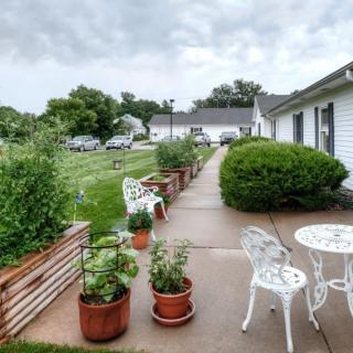 A scenic view of a garden patio with potted plants and outdoor furniture lining a walkway.
