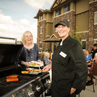 Two people cooking on a grill during an outdoor gathering.