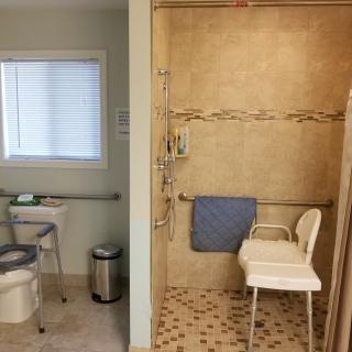 An accessible bathroom featuring a tiled shower with a chair and grab bars, alongside a toilet area with additional support features.