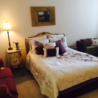 A cozy bedroom interior featuring a neatly made bed with decorative pillows, a bedside table with a lamp, and classic furniture.