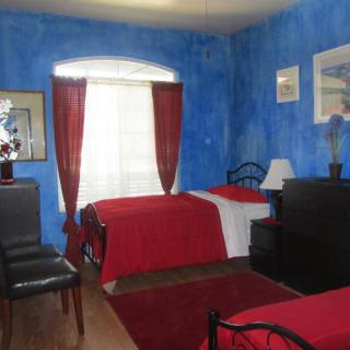 A cozy bedroom with vibrant blue walls and red bedding on two beds, complemented by natural light streaming through the curtains.