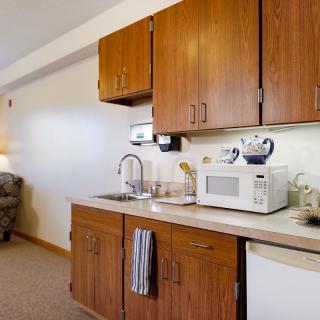 A compact kitchenette with wooden cabinets, a microwave, and a sink.