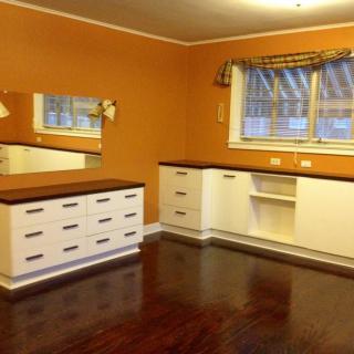 A room with orange walls featuring a white dresser, mirrors, and hardwood flooring.