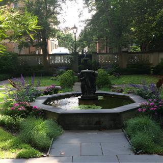 A serene garden with a central fountain surrounded by lush greenery and flowers.