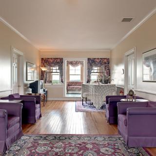 A traditional living room with purple chairs and a wooden floor, featuring a decorative rug and large windows.
