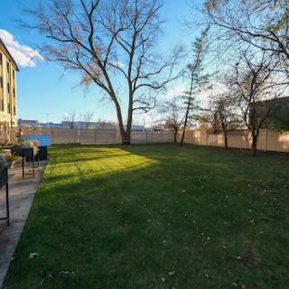 A serene outdoor space featuring a lush green lawn, trees, and a view of the waterfront under a clear blue sky.