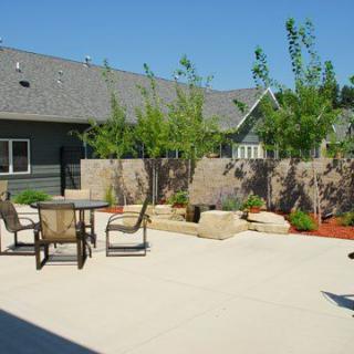 A spacious patio area with outdoor furniture, surrounded by a garden and young trees.