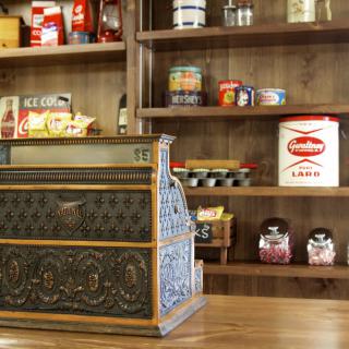 A vintage cash register in an old-fashioned store setting, surrounded by retro items on shelves.