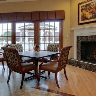 A cozy dining area features a table with four chairs, a fireplace, and large windows letting in natural light.