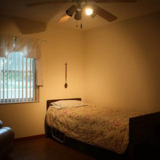 A cozy bedroom featuring a bed, window with curtains, and a ceiling fan.