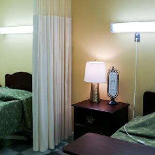 A typical hospital patient room featuring two beds, a separating curtain, and bedside furniture.