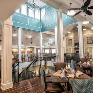 An elegant dining area with natural light, featuring multiple tables and chairs, ceiling fans, and white columns.
