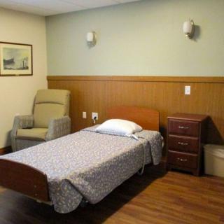 A simple hospital room with a bed, chair, and nightstand.