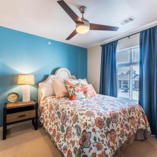 A cozy bedroom featuring floral bedding, blue accent wall, and natural light streaming through the window.