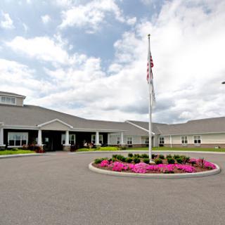 A welcoming entrance to a modern facility, surrounded by vibrant flowers and an American flag.