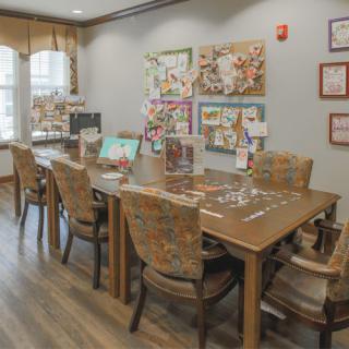 A cozy room with a large table surrounded by chairs, adorned with artwork and puzzles.