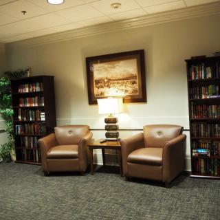 A cozy reading area with leather chairs, bookshelves, and a lamp.