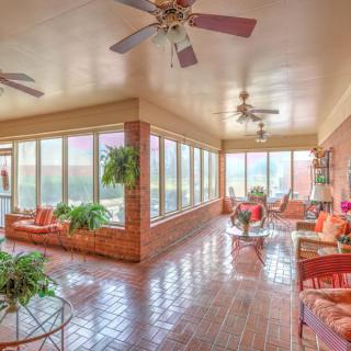 A spacious sunroom filled with natural light, featuring brick walls, cozy furniture, and an array of potted plants.