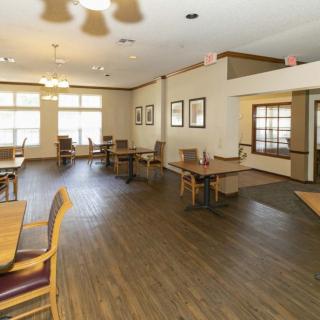 A spacious dining area with wooden floors and several tables and chairs arranged near large windows.
