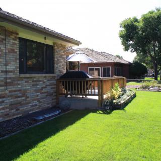 A sunny day view of a house with a lush green lawn and a wooden deck in the backyard.