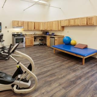 A well-equipped gym area featuring exercise machines, therapy balls, and a padded workout surface.