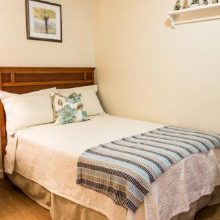 A cozy bedroom with a neatly made bed adorned with pillows and a striped blanket, complemented by wall decor.