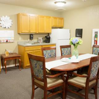 A cozy kitchen and dining area with a wooden table, cushioned chairs, and a flower vase centerpiece.