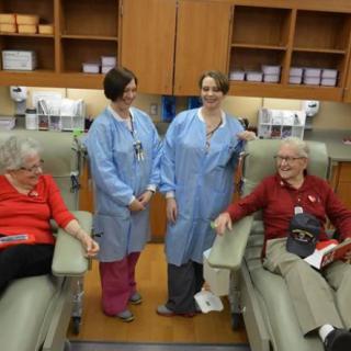 Nurses interact with patients seated in a hospital treatment room.
