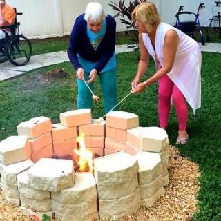 Two people roasting marshmallows over a fire pit in a garden.