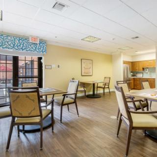 A spacious and bright dining area with several tables and chairs, adjacent to a kitchen.
