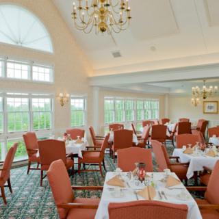 An elegantly decorated restaurant dining room with large windows and chandeliers, featuring neatly arranged tables and chairs.