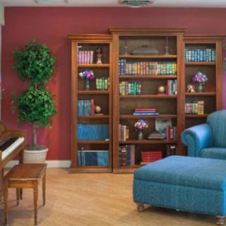 A cozy living room with a bookshelf filled with colorful books, a blue sofa, and a piano against a red wall.