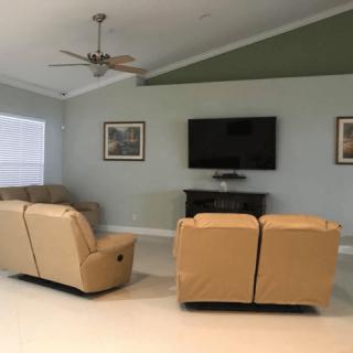 A cozy living room with tan couches facing a wall-mounted television flanked by framed art.