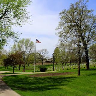 A serene park scene featuring a flag, lush green grass, and trees under a clear blue sky.