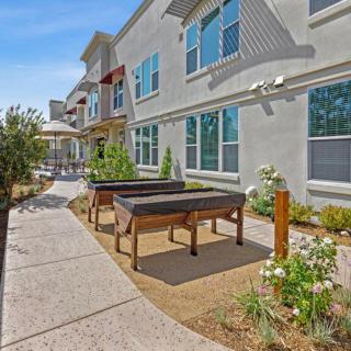 A sunny outdoor area featuring a walkway, foosball tables, and landscaped garden beside a modern building.