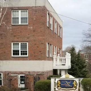 A brick residential building with multiple windows and a decorative sign in front.