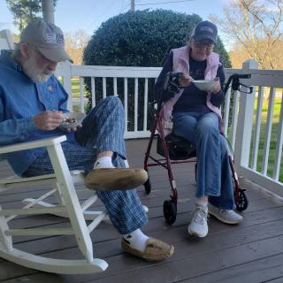 An elderly couple sits leisurely on a porch, enjoying a peaceful moment together.